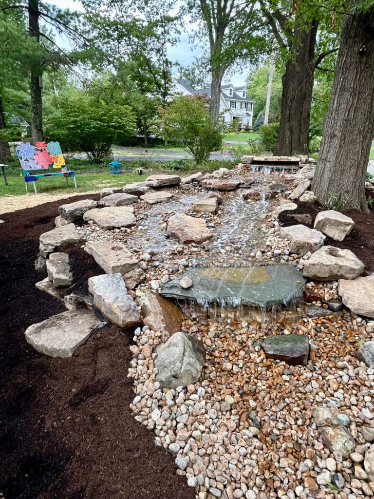 Stone Waterfall Feature Surrounded by Natural Stone Decorative Rock with Trees and Bushes